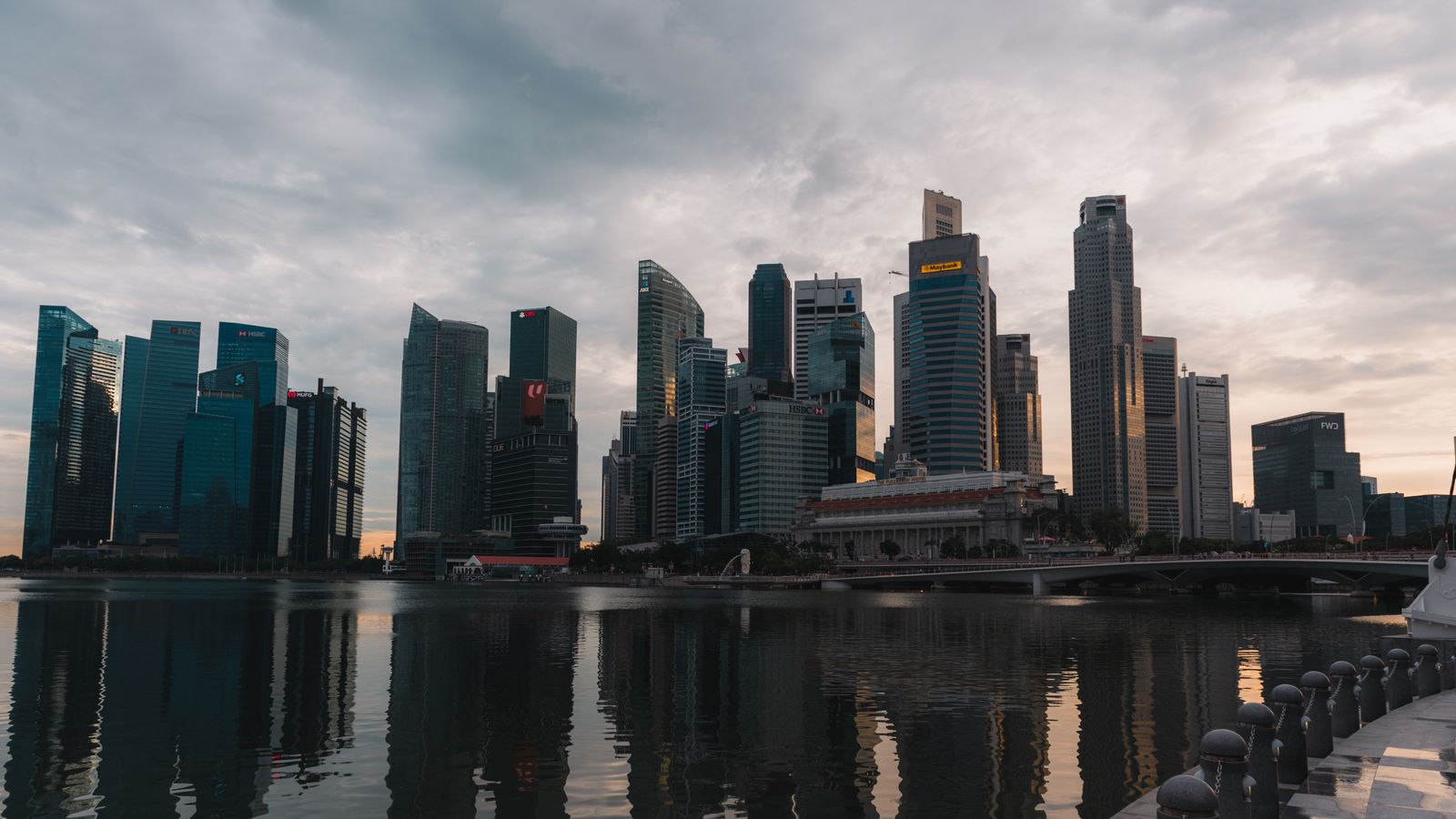 Dramatic skyline of Singapore reflecting on waterfront at dusk with towering skyscrapers.