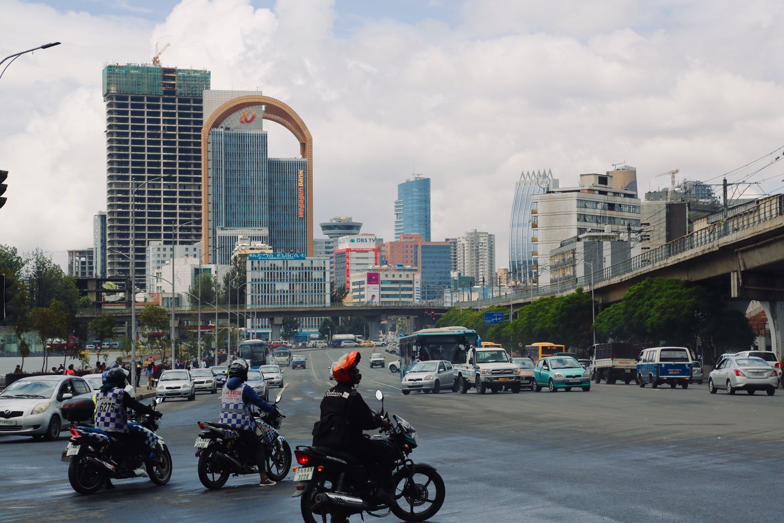 Bikers and cars bustling in Addis Ababa's cityscape with iconic buildings and clear skies.