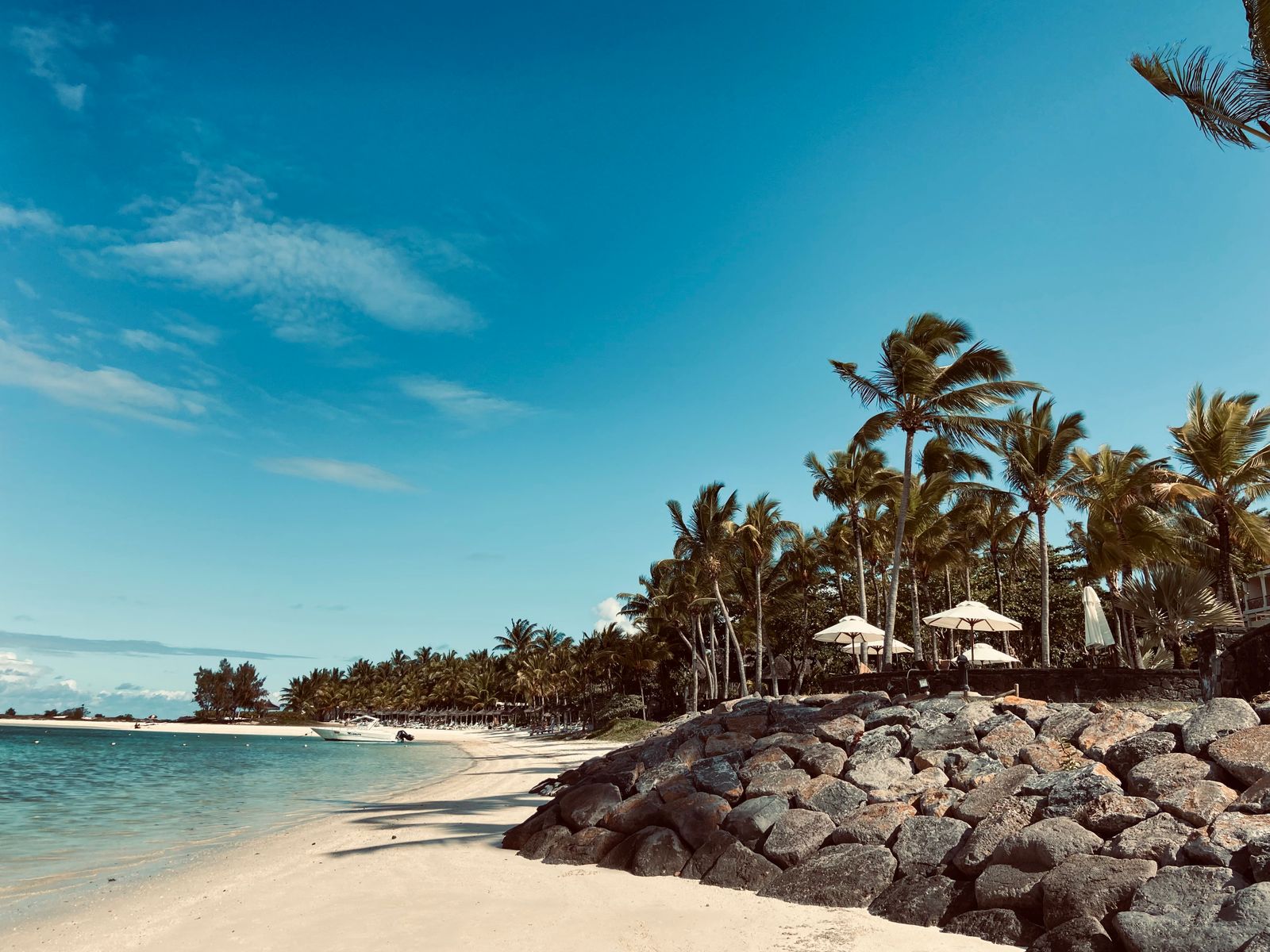 Serene sandy beach in Moka District, Mauritius, with clear blue skies and lush palm trees.