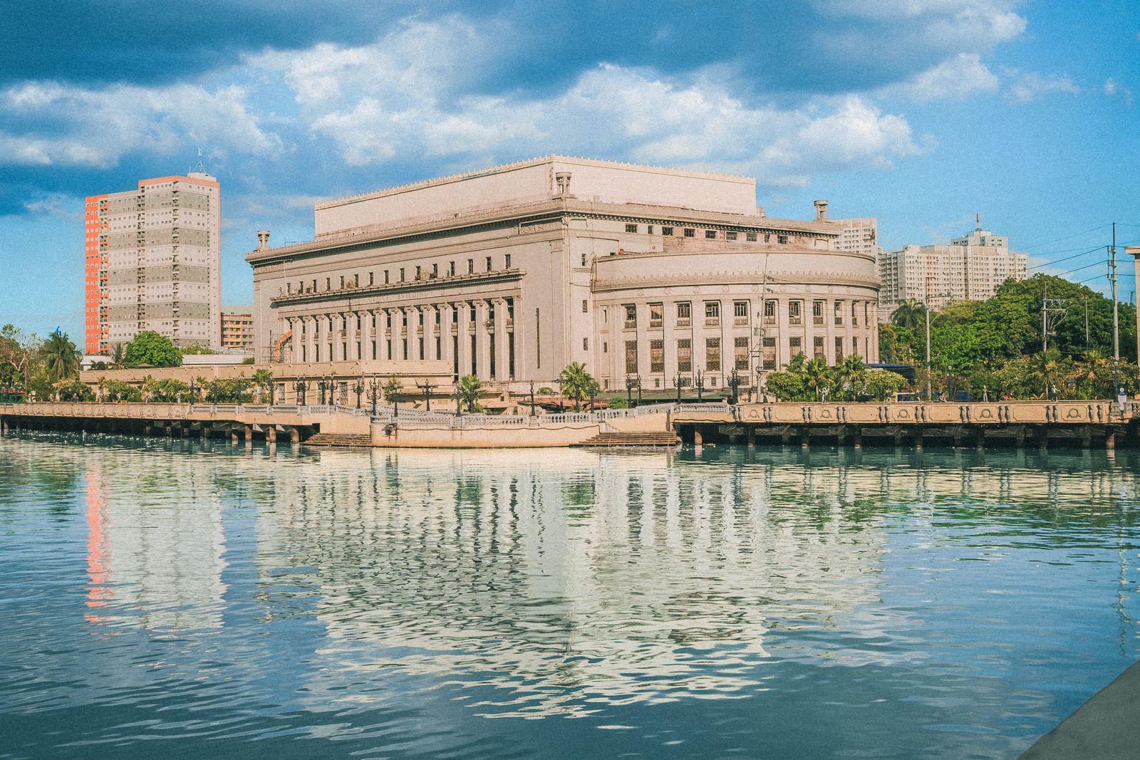 The iconic Manila Post Office building reflecting on the Pasig River under a bright blue sky.